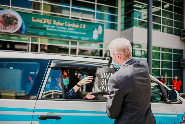 Professor John Wilson (right) distributing containers of bubur lambuk to a representative from Borneo Medical Centre.